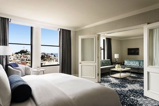 Spacious hotel room with a large bed, sitting area, and city view through wide windows