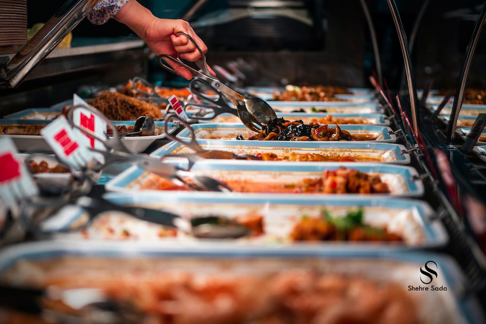 A person serving food from a buffet counter with multiple dishes on display